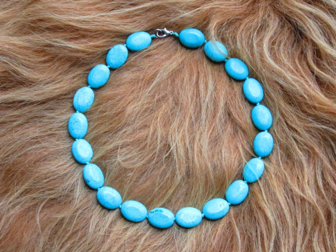 Blue and turquoise beaded bracelet with round polished stones arranged in a circle on textured neutral fabric background