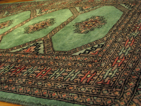 Green handwoven textile with intricate red and gold traditional patterns, folded to show Central Asian fabric detail