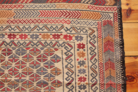 Close-up of woven textile featuring geometric patterns in red, cream, and blue with traditional border design