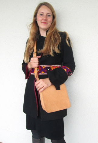 Femme portant un blazer noir et un sac à bandoulière orange en cuir artisanal, vue de face