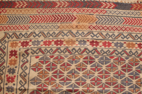 Handwoven textile in red and cream with geometric diamond pattern and decorative border, flat lay view