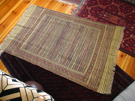 Handwoven textile with striped pattern in natural and grey tones, displayed on dark fabric