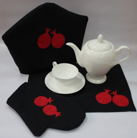 Black textile with red pomegranate embroidery displayed with white ceramic teapot and cup, flat lay arrangement