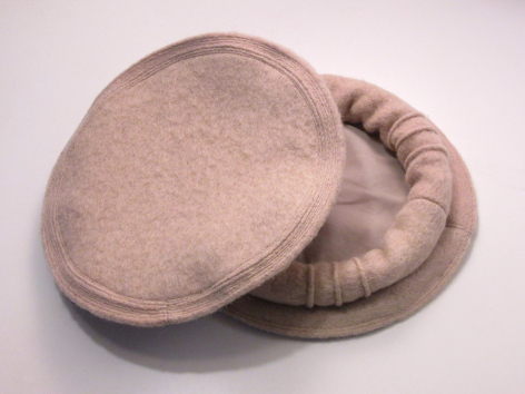 Coussin rond en laine beige clair, vue de trois-quarts montrant la texture tissée et les coutures sur les bords