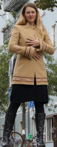 Woman wearing tan wool-blend tunic sweater with black leggings and brown leather bag, standing with bicycle