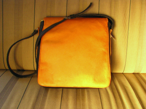 Bright golden-yellow square fabric pouch with black cord handles, displayed flat on wooden surface