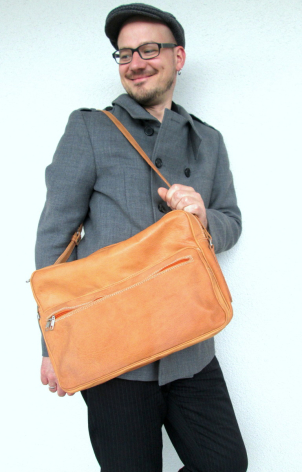 Person holding an orange leather crossbody bag with brown shoulder strap, front view