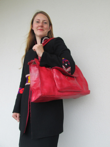 Woman wearing black blazer holding bright red leather tote bag with black accents, front view