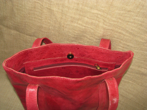 Red leather tote bag open to show interior compartments and dual handles, viewed from above