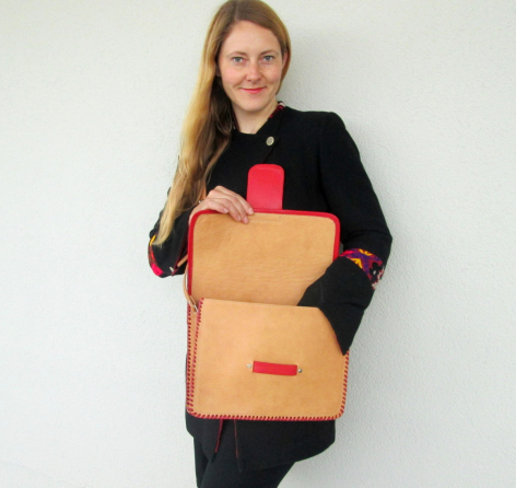 Woman holding tan leather backpack with red accents and front pocket, worn over black jacket