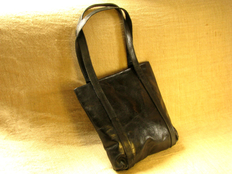 Petit sac à main en cuir noir avec poignées, vue de dessus sur fond doré