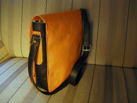 Sac en cuir orange avec rabat et sangle noire, vue de trois quarts sur fond de bois clair