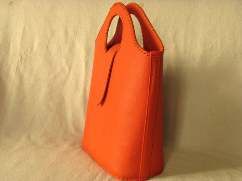 Sac à main de forme cylindrique en cuir orange vif, vue de côté avec poignées noires