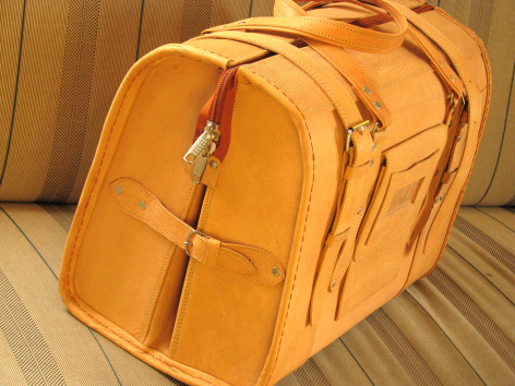 Sac à dos en cuir tanné orange avec poches frontales et bretelles, vue de trois quarts sur fond de bois clair