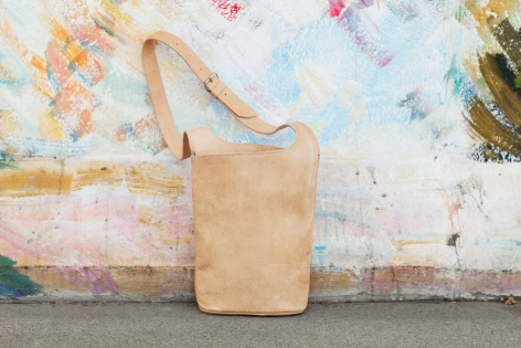 Petit sac à bandoulière en cuir beige clair avec lanière longue, vue de face sur surface texturée