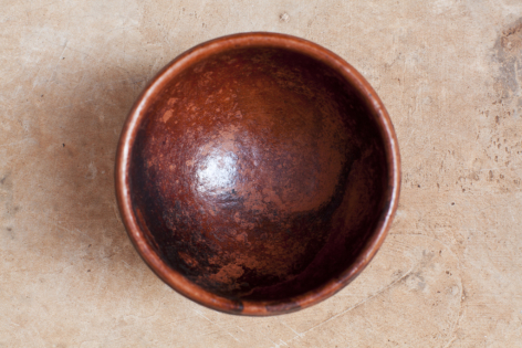 Handcrafted copper bowl with deep patina, viewed from above showing smooth curved interior and polished rounded base