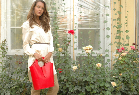 Woman wearing cream top and red leather bag standing in front of ivy-covered wall with green plants