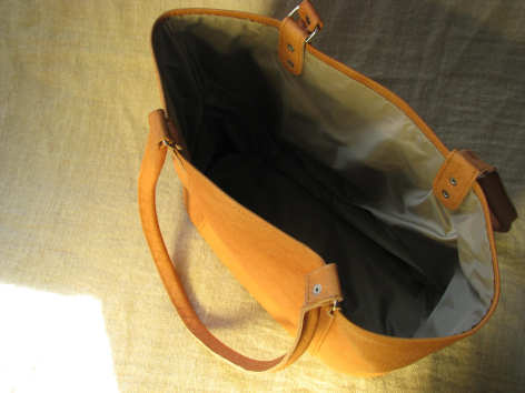 Golden-tan leather tote bag shown open from above, displaying black fabric interior and dual handles