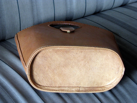 Brown leather pouch with rounded rectangular shape and cream suede interior detail, front view on blue fabric surface