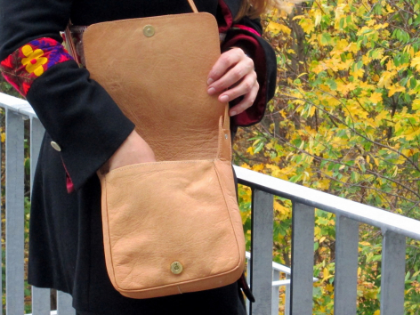Person holding tan leather shoulder bag with floral patterned textile background