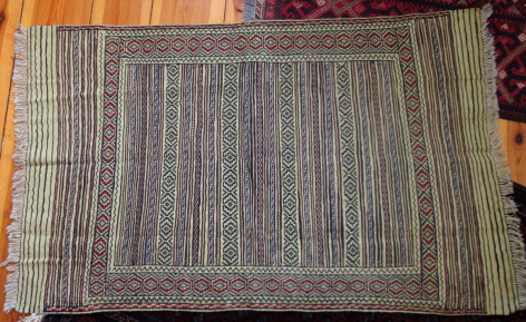 Tapis tissé à motifs géométriques rayés en tons gris et bleu, vue de dessus sur sol en bois