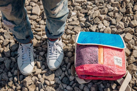 Person wearing patterned socks standing on gravel next to a small colorful woven pouch in blue and red