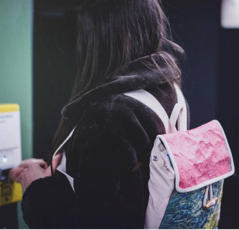 Person wearing black jacket viewed from behind, holding pink patterned textile or fabric sample against their body