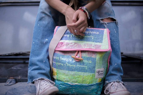 Person wearing jeans holding a colorful striped woven textile bag in green, pink, and blue tones