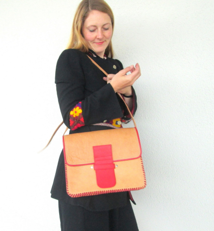 Frau trägt schwarze Kleidung und hält eine orange-rote Ledertasche mit geometrischen Farbblöcken über der Schulter