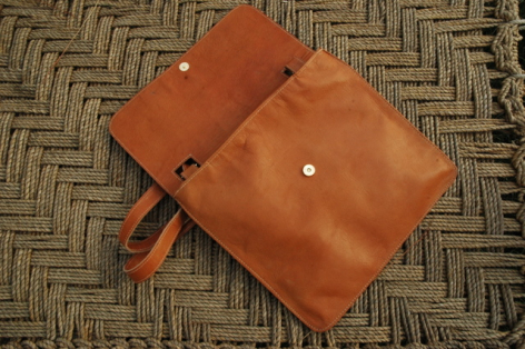Tan leather crossbody bag with front flap closure and side strap, displayed open on patterned textile surface
