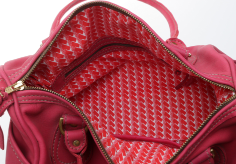Red leather handbag open to show patterned fabric lining inside with handles visible at top