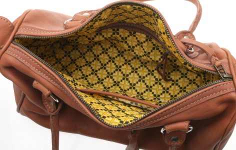 Tan leather tote bag open to show yellow patterned fabric lining interior, viewed from above at angle