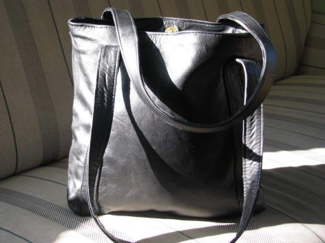 Sac à main en cuir noir avec anses, vue de face, posé sur siège clair