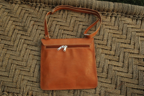 Cognac brown leather shoulder bag with structured rectangular shape and silver clasp, on woven textile