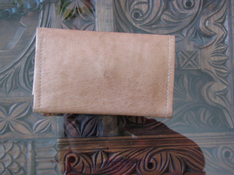 Tan leather clutch with suede finish displayed above carved wooden box on patterned textile
