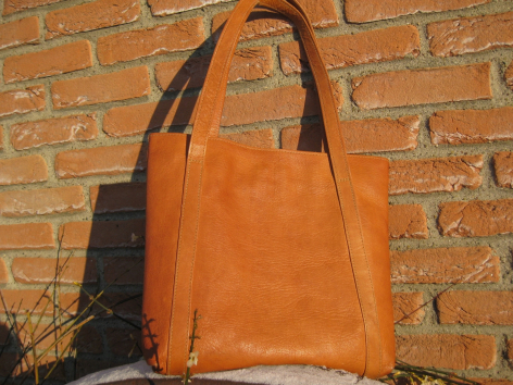 Orangefarbene Ledertasche mit Henkeln, Vorderansicht, vor Backsteinmauer, handwerklich verarbeitet