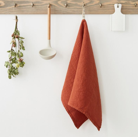 Rust-red linen towel hanging from wooden rail with dried herb bundle and ceramic dish beside it