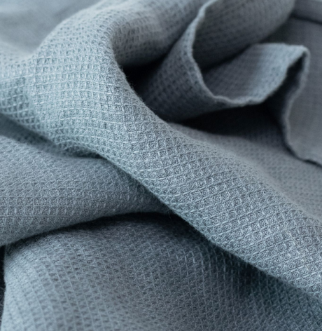 Close-up of folded blue-grey woven textile with textured surface and soft, draped folds