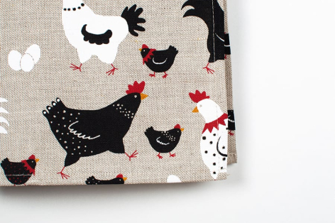 Cream textile with black and red rooster and chicken print pattern, folded corner detail view