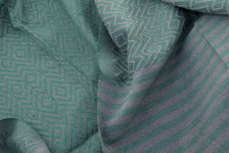 Close-up of folded teal and grey woven textiles showing contrasting geometric patterns and natural fabric texture