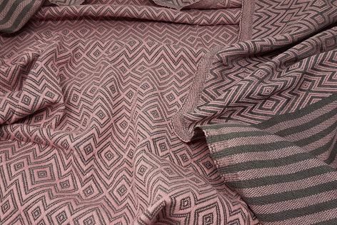 Close-up detail of folded textiles showing woven geometric and striped patterns in muted mauve and gray tones