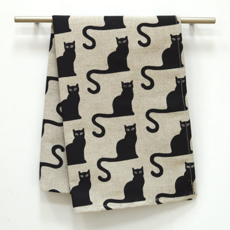Cream linen textile with black cat silhouettes and S motifs, draped over wooden rod, folded display