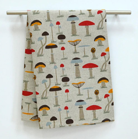 Cream linen textile featuring scattered red and yellow mushroom illustrations in repeating pattern, hung on wooden rod