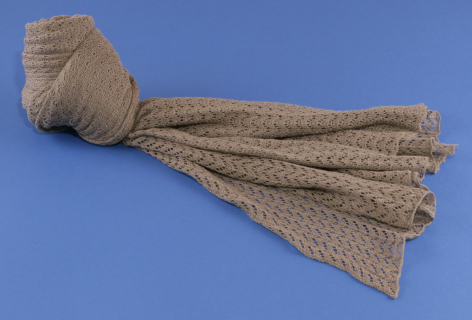 Beige linen tassel with knotted head and fringed skirt, displayed against blue background