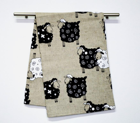 Cream and black patterned textile folded over metal rod, featuring repeated cat face motifs with white accents