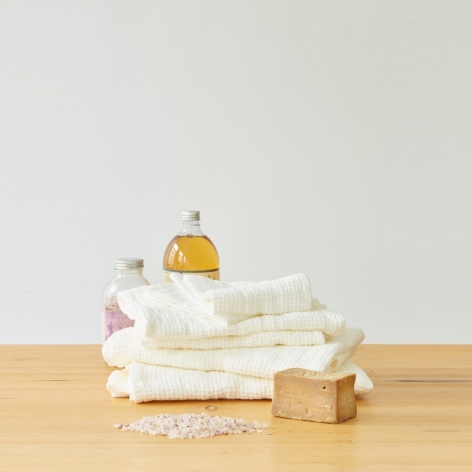 Folded cream and white textiles stacked on wooden surface with brass bell on top and natural fiber accents