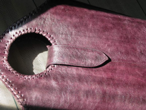 Burgundy velvet textile detail showing hand-stitched seam and metal hook closure against dark background