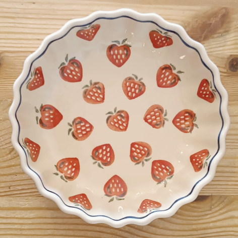 Cream ceramic bowl with scalloped rim and red strawberry pattern throughout, top view