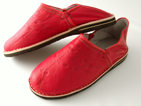 Pair of red velvet slip-on slippers with dark brown leather trim and soles, displayed at three-quarter angle