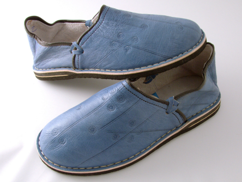 Pair of blue suede slippers with brown leather trim and natural sole, angled view showing side profile